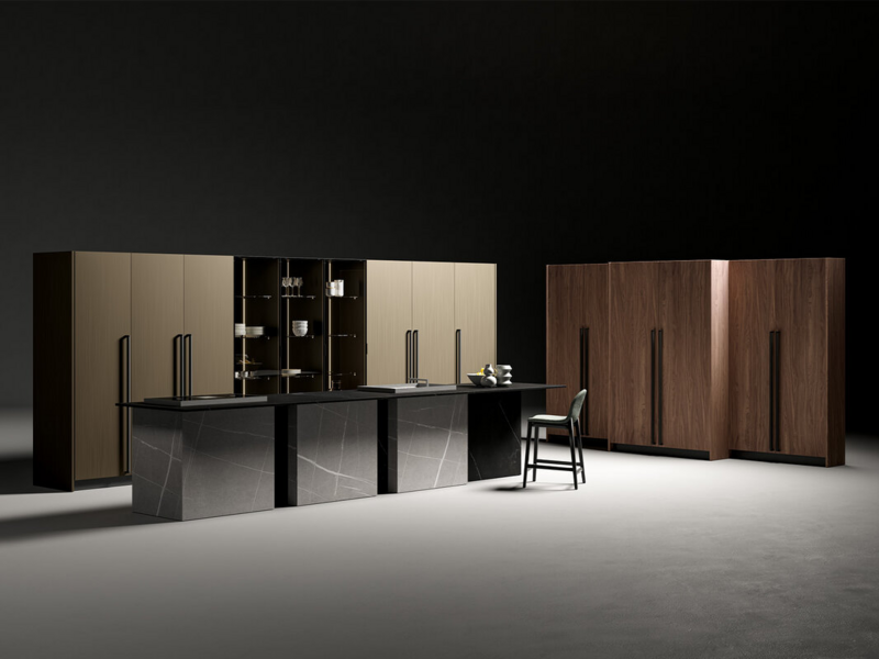 Island in matt lacquered nero with handle. Back panels, sides and worktop in stoneware Gris Natural Senda and Negro Natural Storm. Tall units in Canaletto walnut wood and satin metal lacquered ottone with handle. Tall units vidro CX 19 with matt lacquered nero structure and smoked glass.