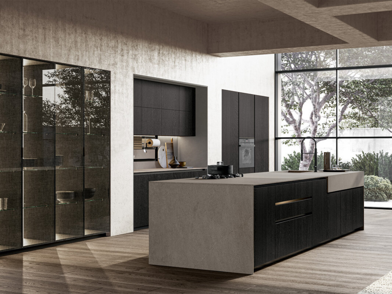 Base and tall units CX 11 in carbon oak wood with black curved groove. Back panels, side panels and worktop in stoneware Moka Abujardado Jasper. Vidro tall units CX 19 with black aluminium frame and smoked glass with fabric effect.